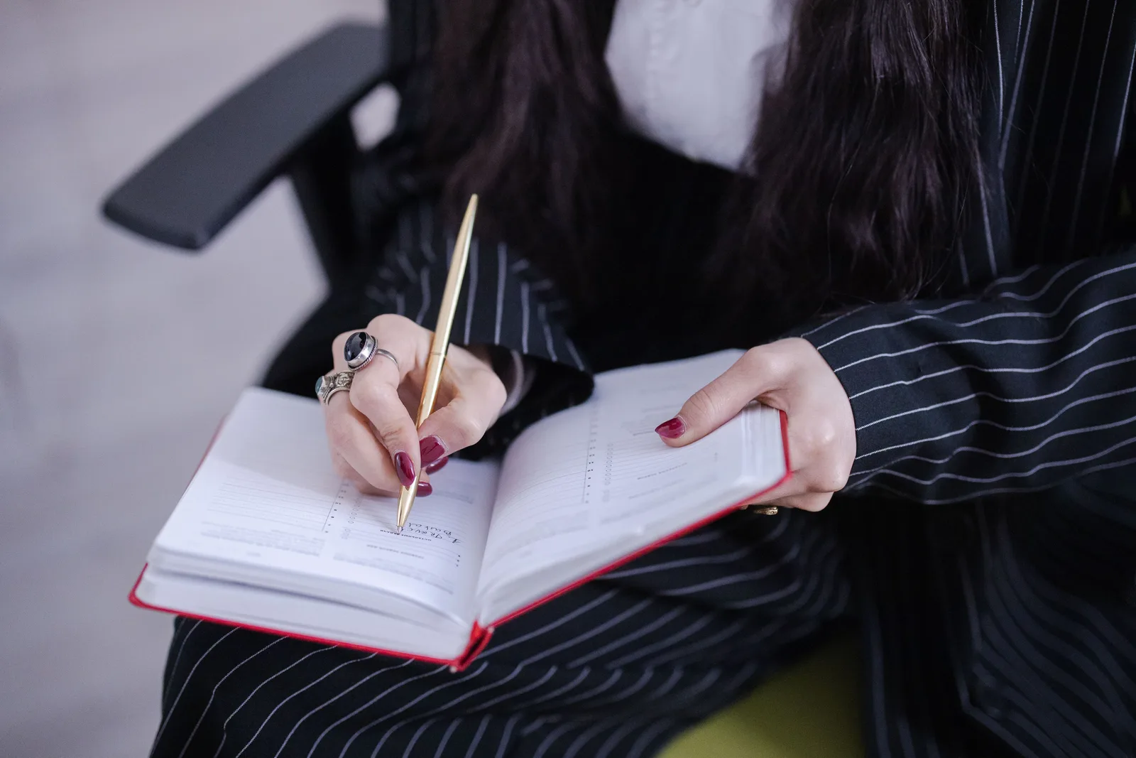 A woman in a pinstripe suit writing notes in a planner with a gold pen. Mobile notary service standards: a drafting method