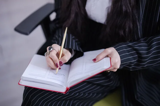 A woman in a pinstripe suit writing notes in a planner with a gold pen. Mobile notary service standards: a drafting method