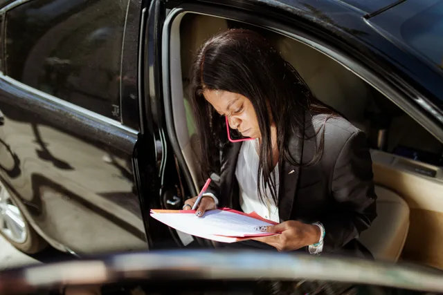 A focused businesswoman analyzes documents while sitting in her car. Mobile notary business operations: filing IRS Schedule C