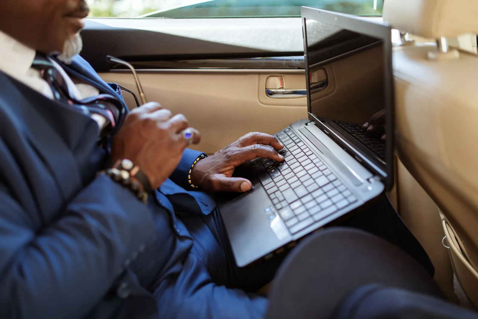 Close-up of a businessman typing on a laptop in a car interior during travel. Mobile notary bookkeeping: a weekly cash routine