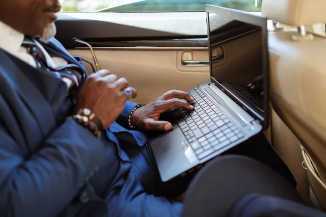 Close-up of a businessman typing on a laptop in a car interior during travel. Mobile notary bookkeeping: a weekly cash routine