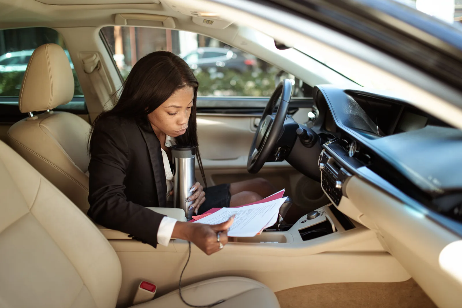 A focused businesswoman reads documents in her car, multitasking with a tumbler. Mobile notary business plan: a formula framework