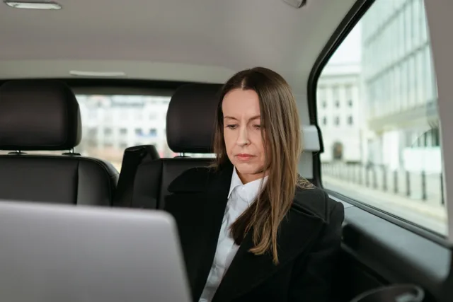 Focused businesswoman in formal attire working on a laptop in the back seat of a car. Mobile Notary E&O Insurance Requirements: When They Apply