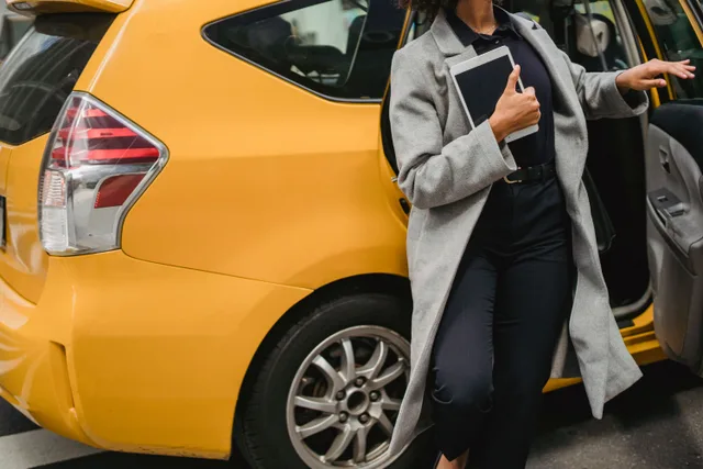 Crop unrecognizable female in formal clothes holding tablet while getting out of yellow taxi. Mobile notary marketing: three channels and trade-offs