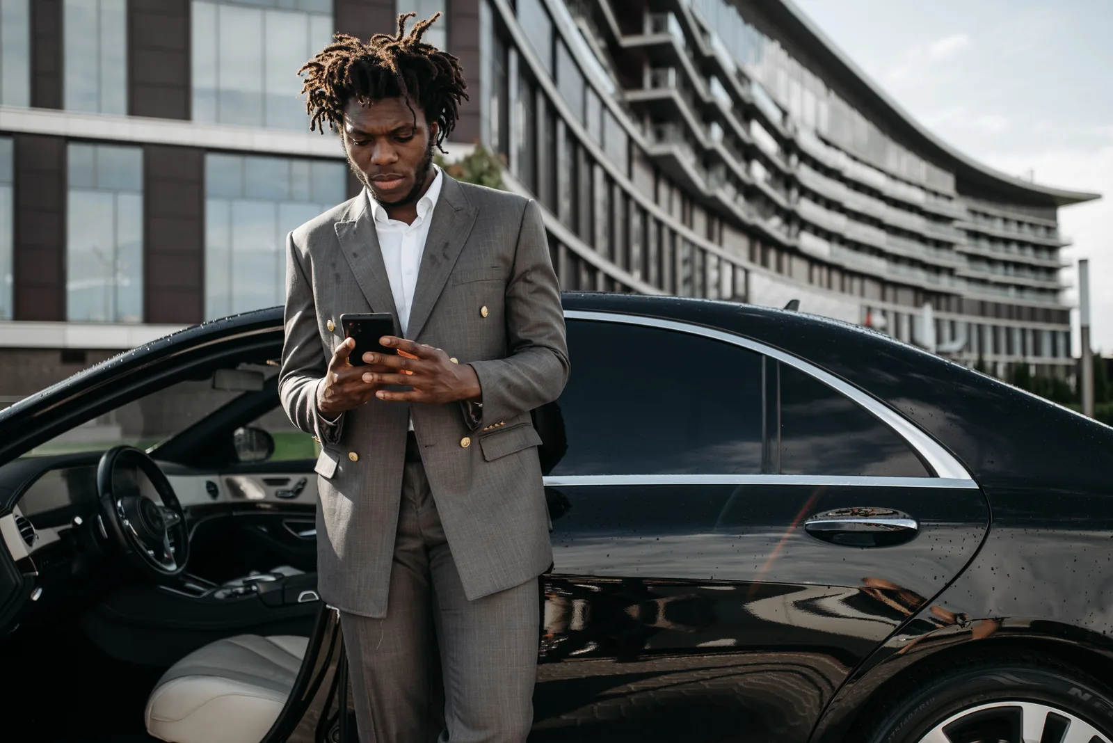 Professional man in a gray suit using his phone next to a luxury car. Mobile Notary Pricing: Set a Cost-Based Travel Fee