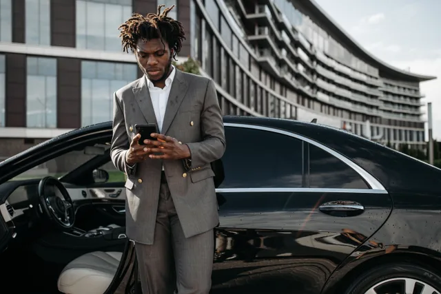 Professional man in a gray suit using his phone next to a luxury car. Mobile Notary Pricing: Set a Cost-Based Travel Fee