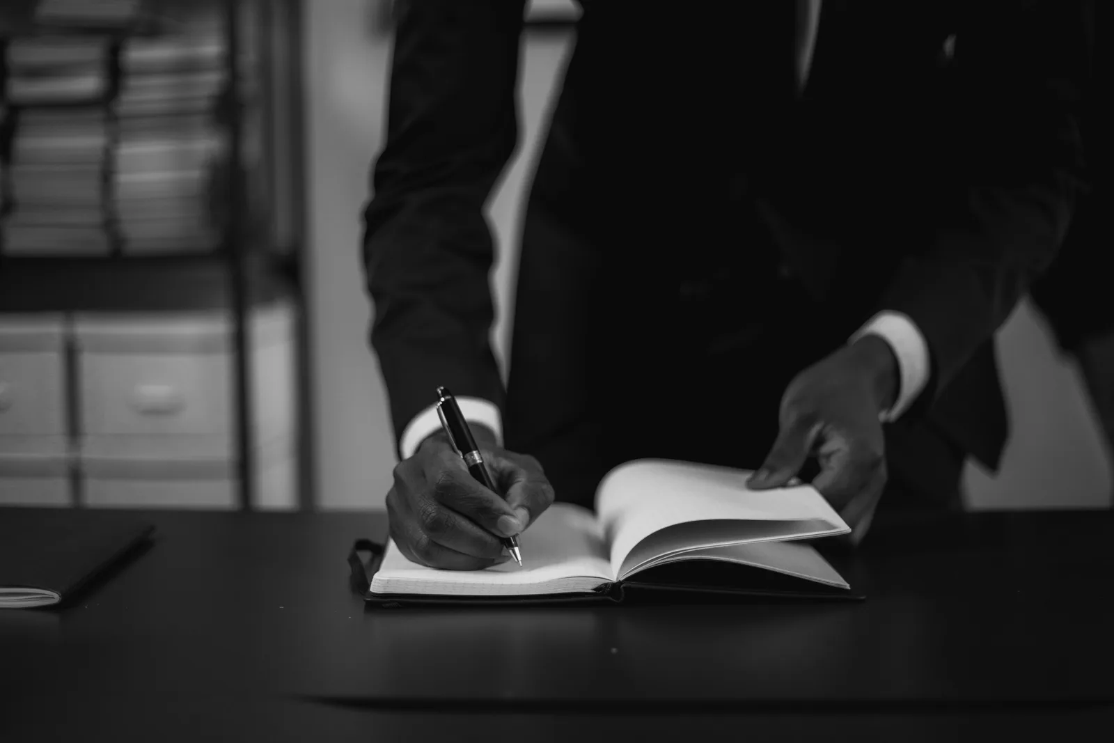 Monochrome image of a businessman in a suit writing in a notebook at a desk. Top mobile notary services, rated on evidence rather than hype