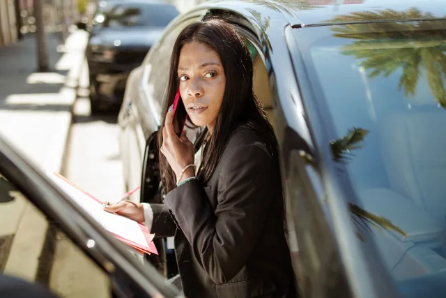 Confident businesswoman in corporate attire multitasking with a phone call and notes in a car. Measuring profitable mobile notary services
