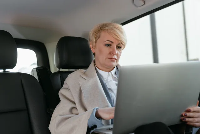 Professional woman with short hair using a laptop in a car interior. Which US states see mobile notary demand spike at tax season?